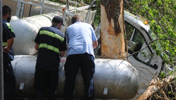 Officials work to empty a propane tank that was tossed off the truck that was hauling it after the truck exited the highway and collided with a tree Monday afternoon on Ala. Hwy. 185. (Advocate Staff/Andy Brown)