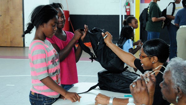 Zamaria McCall (left) and Zari Brown (right) accept book bags from volunteers Karen Owens and Lillian Herbert during last year's book bag giveaway. This year's event is set for Aug. 3 at the Greenville YMCA. (File Photo)