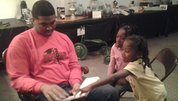 Jaeques Brown reads to a pair of children who attended the 2014 Black History Exhibit at the Robinson Activity Center. This year’s theme, “Riding into the Past,” features a collection of bicycles and tricycles, as well as other means of entertainment for black children in an age before television and the Internet. (Courtesy Photo)